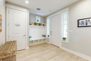A hallway with white doors, a wicker bench, a utility room sign, and a framed picture on the wall. - Palmilla Beach Resort-197 Sunset Avenue (Port Aransas)