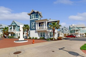 A residential area with multiple two-story houses featuring gabled roofs and balconies, a central circular driveway, and a red vehicle parked on the street. - Palmilla Beach Resort-198 Sage Lane (Port Aransas)