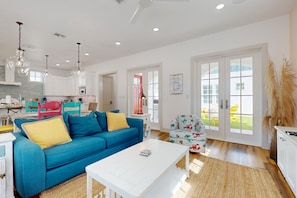 A spacious living room with a blue sofa, a white coffee table, and a kitchen in the background. - Palmilla Beach Resort-198 Sage Lane (Port Aransas)