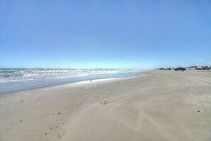 A beach with a clear sky, a sandy shore, and a few vehicles parked on the right. - Palmilla Beach Resort-200 Sunset Avenue (Port Aransas)