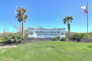 A sign for Palmilla Beach Resort & Golf Community with palm trees and a flag. - Palmilla Beach Resort-200 Sunset Avenue (Port Aransas)