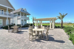 A patio with outdoor furniture and a pergola, a large house with a balcony, and a golf course in the background. - Palmilla Beach Resort-200 Sunset Avenue (Port Aransas)