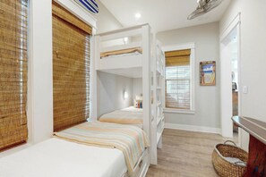 A room with bunk beds, a window with a beach-themed poster, and a woven basket on the floor. - Palmilla Beach Resort-204 Sunset Avenue (Port Aransas)