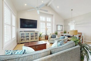 A spacious living room with a high ceiling, a television, a sofa, a coffee table, and a dining area with a table and chairs. - Palmilla Beach Resort-204 Sunset Avenue (Port Aransas)