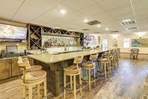 Eine Bar mit einer langen Theke, mehreren Hockern und einem Fernseher, der eine Wrestling-Veranstaltung zeigt.