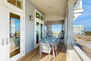 A covered outdoor area with a wooden table and chairs, a spiral staircase, and a view of a building in the background. - Palmilla Beach Resort-218 Sunrise Avenue (Port Aransas)