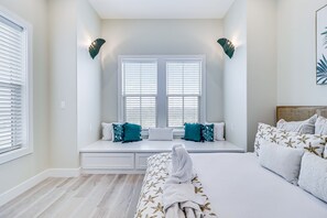 Ein Schlafzimmer mit großem Fenster, einem Bett mit weißer Bettwäsche und einer Sitzbank mit Kissen.