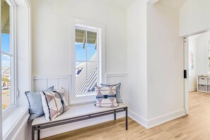 A room with a bench against a wall, a window with blinds, and a door leading to another room. - Palmilla Beach Resort-220 Sunrise Avenue (Port Aransas)