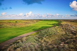 Een golfbaan met een duidelijke route, open gazons en verre gebouwen.
