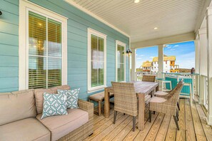 A covered porch with a wooden floor, a table with chairs, and a sofa with patterned cushions. - Palmilla Beach Resort-222 Sundew Lane (Port Aransas)