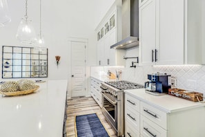 A modern kitchen with white cabinetry, a central island, a gas stove, and a coffee machine. - Palmilla Beach Resort-222 Sundew Lane (Port Aransas)