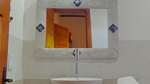 A bathroom with a white sink, a mirror with decorative frame, and a towel basket. - Pousada Luar de Pitinga (Arraial d'Ajuda)