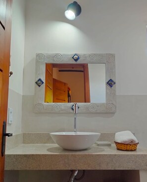 A bathroom with a white sink, a mirror with decorative frame, and a towel basket. - Pousada Luar de Pitinga (Arraial d'Ajuda)