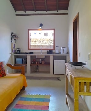 A compact room with a bed, a small desk, a window, and a kitchenette. - Pousada Luar de Pitinga (Arraial d'Ajuda)