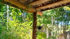 An outdoor wooden deck with a table and chairs, surrounded by lush greenery and trees. - Pousada Luar de Pitinga (Arraial d'Ajuda)