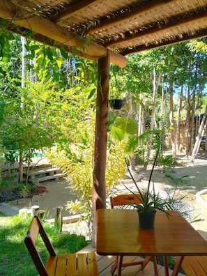 An outdoor wooden deck with a table and chairs, surrounded by lush greenery and trees. - Pousada Luar de Pitinga (Arraial d'Ajuda)