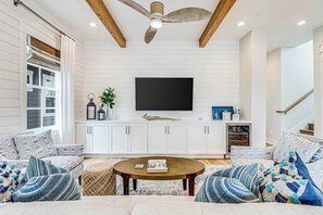 Ein Wohnzimmer mit Deckenventilator, weißen Schränken, einem Flachbildfernseher und gemusterten Kissen.
