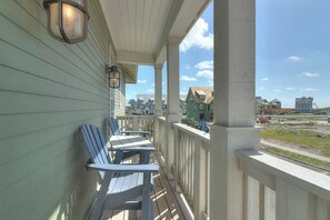 A porch with two Adirondack chairs, a railing, and a view of houses in the background. - Palmilla Beach Resort-226 Sunset Avenue (Port Aransas)