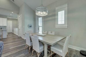 A dining area with a light-colored table and wicker chairs, a hanging light fixture, and a view of the kitchen in the background. - Palmilla Beach Resort-226 Sunset Avenue (Port Aransas)