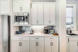 A modern kitchen with white cabinets, a stainless steel refrigerator, a microwave, a coffee maker, and a toaster. - Palmilla Beach Resort-228 Sunrise Avenue (Port Aransas)