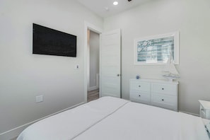 Ein Schlafzimmer mit einem Bett, einer weißen Kommode, einem gerahmten Bild und einer Tür zu einem anderen Raum.