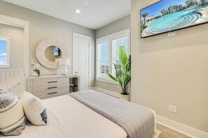 A bedroom with a bed, a dresser, a mirror, a television, and a window with blinds. - Palmilla Beach Resort-236 Sunset Avenue (Port Aransas)