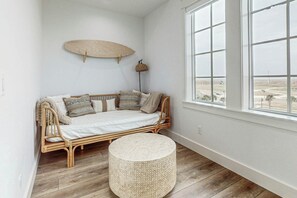 A room with a rattan sofa, a round woven ottoman, and a large window with a view of a landscape. - Palmilla Beach Resort-250 Sunrise Avenue (Port Aransas)