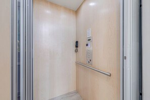 A narrow elevator with a control panel, a handrail, and a door with a glass panel. - Palmilla Beach Resort-250 Sunset Avenue (Port Aransas)