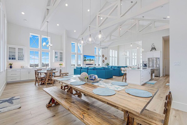 A spacious kitchen with a long wooden table, white cabinetry, and a view of the outdoors. - Palmilla Beach Resort-250 Sunset Avenue (Port Aransas)
