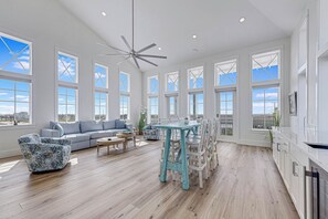 A spacious living area with a large sofa, a dining table, and a ceiling fan. - Palmilla Beach Resort-250 Sunset Avenue (Port Aransas)