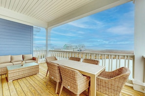 A covered outdoor area with a wooden deck, wicker furniture, and a view of houses across the water. - Palmilla Beach Resort-254 Sunrise Avenue (Port Aransas)