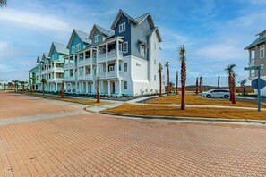 A multi-story residential building with a prominent balcony on the second floor, a paved driveway, and palm trees lining the street. - Palmilla Beach Resort-254 Sunrise Avenue (Port Aransas)