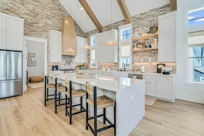 A modern kitchen with a large island, white cabinetry, and a brick wall. - Palmilla Beach Resort-260 Sunrise Avenue (Port Aransas)