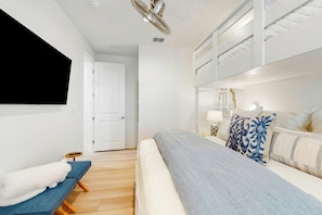 A modern bedroom with a bunk bed, a flat-screen TV, a bedside table with a lamp, and a window with blinds. - Palmilla Beach Resort-280 Sunrise Avenue (Port Aransas)