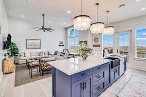 A spacious living area with a large island, a dining table, and a ceiling fan. - Palmilla Beach Resort-284 Sunrise Avenue (Port Aransas)