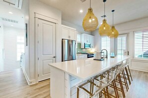Una cocina moderna con una isla central, electrodomésticos de acero inoxidable e iluminación colgante.