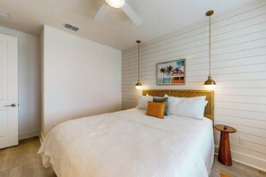 Een slaapkamer met een bed, een nachtkastje, een schilderij en een plafondventilator.