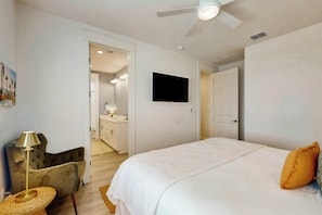 A bedroom with a bed, a television, a ceiling fan, and a door leading to a bathroom. - Palmilla Beach Resort-288 Sunrise Avenue (Port Aransas)