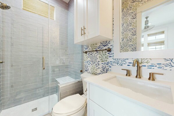 A bathroom with a glass shower enclosure, a white toilet, and a sink with a mirror above it. - Palmilla Beach Resort-300 Mermaid Tail Lane (Port Aransas)
