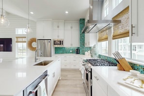 A modern kitchen with white cabinetry, a stainless steel refrigerator, a microwave, and a gas stove. - Palmilla Beach Resort-300 Mermaid Tail Lane (Port Aransas)