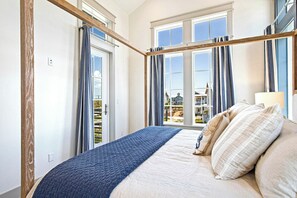 A bedroom with a large bed, a window with curtains, and a view of houses outside. - Palmilla Beach Resort-308 Horse Tail Lane (Port Aransas)