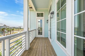 A wooden deck with a white railing, a door with a glass panel, and a light fixture on the wall. - Palmilla Beach Resort-308 Horse Tail Lane (Port Aransas)
