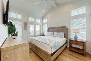 A bedroom with a bed, bedside tables, a desk, a ceiling fan, and large windows. - Palmilla Beach Resort-312 Mermaid Tail Lane (Port Aransas)