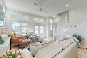 A spacious living room with a high ceiling, a ceiling fan, and a staircase leading to an upper level. - Palmilla Beach Resort-316 Mermaid Tail Lane (Port Aransas)