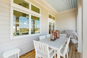 A covered patio with a white table and chairs, large windows, and a view of the landscape. - Palmilla Beach Resort-316 Mermaid Tail Lane (Port Aransas)