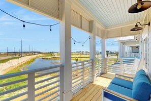 A covered outdoor area with a wooden deck, white railings, and a blue cushioned seating area. - Palmilla Beach Resort-316 Mermaid Tail Lane (Port Aransas)