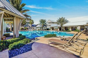 Ein Poolbereich mit Liegestühlen, einer überdachten Lounge und einem Gebäude mit mehreren Balkonen.
