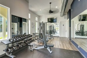 Ein Fitnessstudio mit Krafttrainingsgeräten, Spiegeln und einem Fernseher an der Wand.