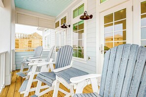A covered outdoor seating area with Adirondack chairs and a table, wooden floors, and a view of a building in the background. - Palmilla Beach Resort-416 Mermaid Tail Lane (Port Aransas)