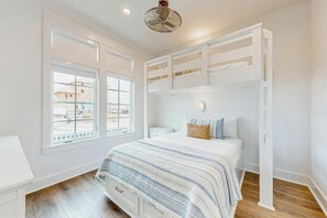 Un dormitorio con literas, una mesita de noche, una lámpara y una ventana con vistas a edificios.